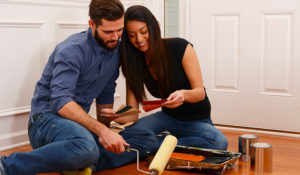 Couple sitting on the floor looks at paint chips in preparation for painting the white walls behind them.